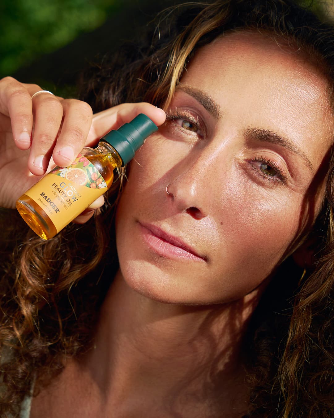 Woman holding Badger Radiant Glow Beauty Oil close-up — natural sunlit skincare photography | Black Rabbit Creative
