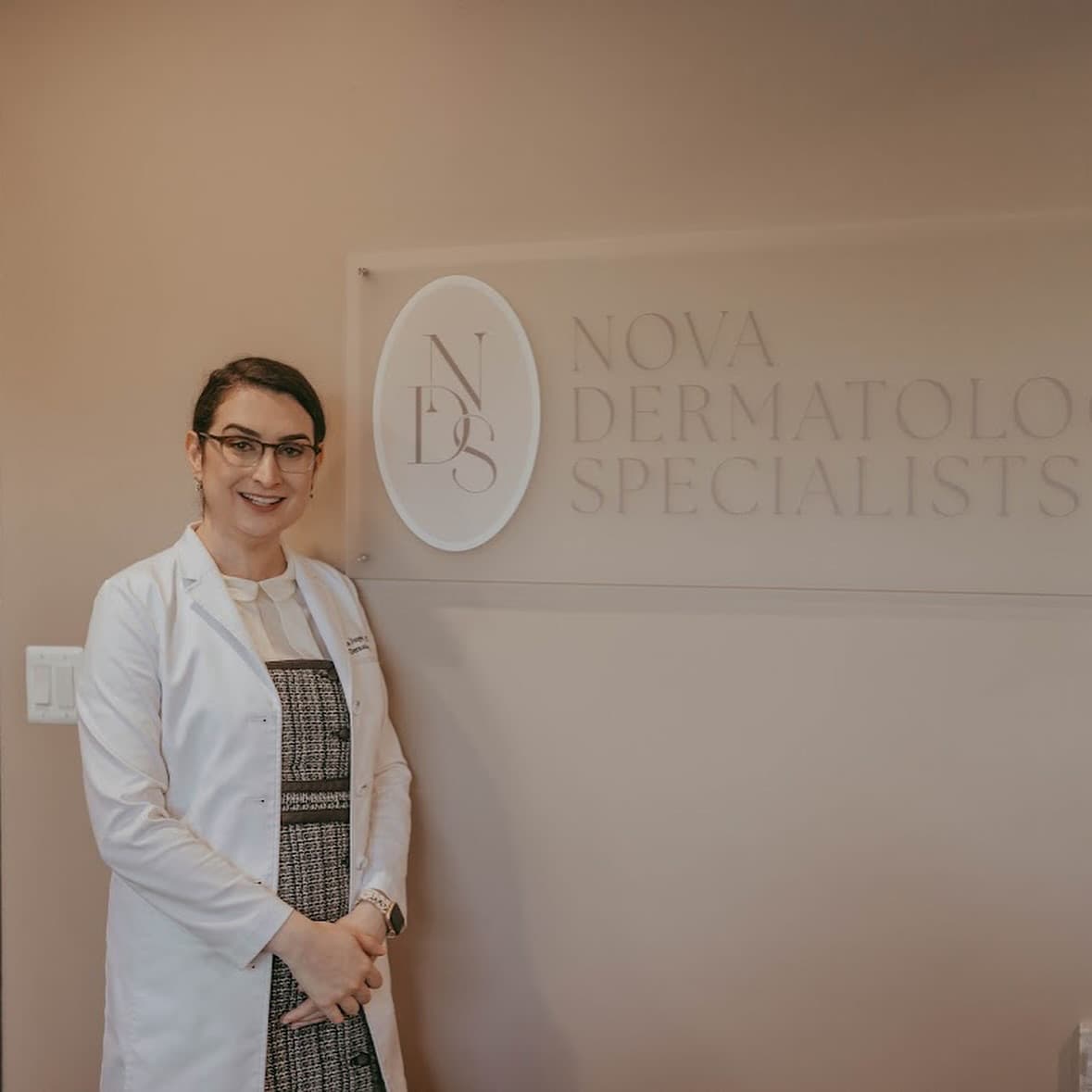 Dr. Marina Jungwirth with Nova Dermatology branded wall signage — brand identity by Black Rabbit Creative